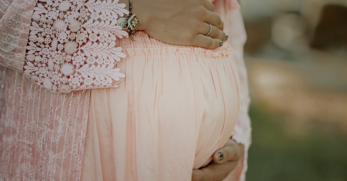 Gestante com 17 semanas abraçando a barriga em vestido rosa claro